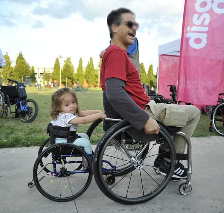 Papa et fille sur fauteuil roulant, l'une derrière l'autre, lui heureux et elle... sans commentaire