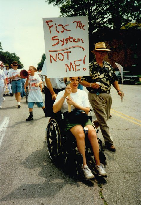 Manifestation publique... Jeune femme en fauteuil roulant portant une pancarte Fix The System... Not Me